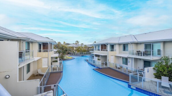 A swimming pool surrounded by multi-story buildings with balconies and outdoor seating areas.