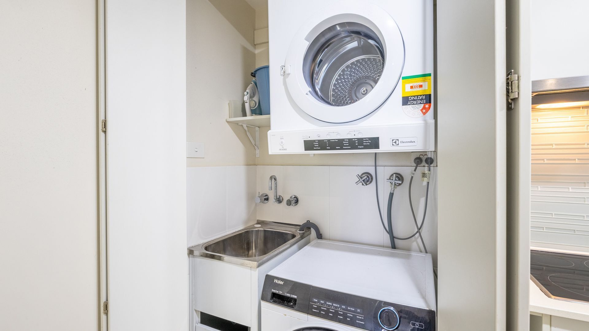 A compact laundry area with a front-loading washer and dryer, a sink, and a small shelf.
