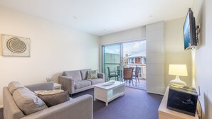 A modern living room with a grey sofa, a white coffee table, and a flat-screen TV mounted on the wall.