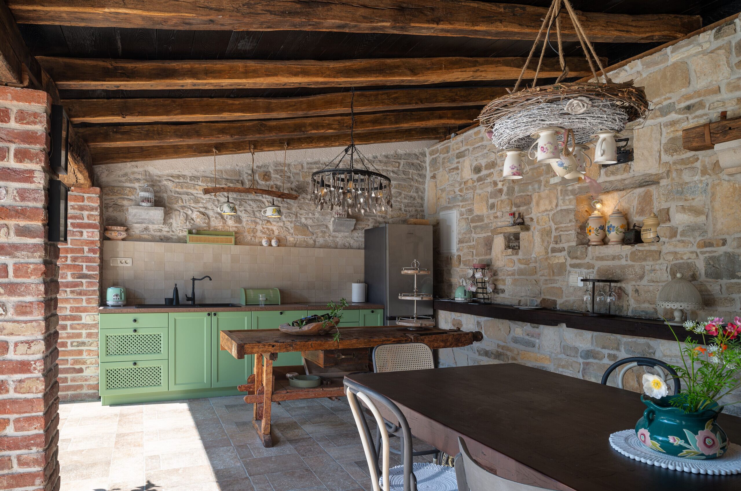A rustic kitchen with exposed brick walls, wooden beams, and a hanging light fixture.