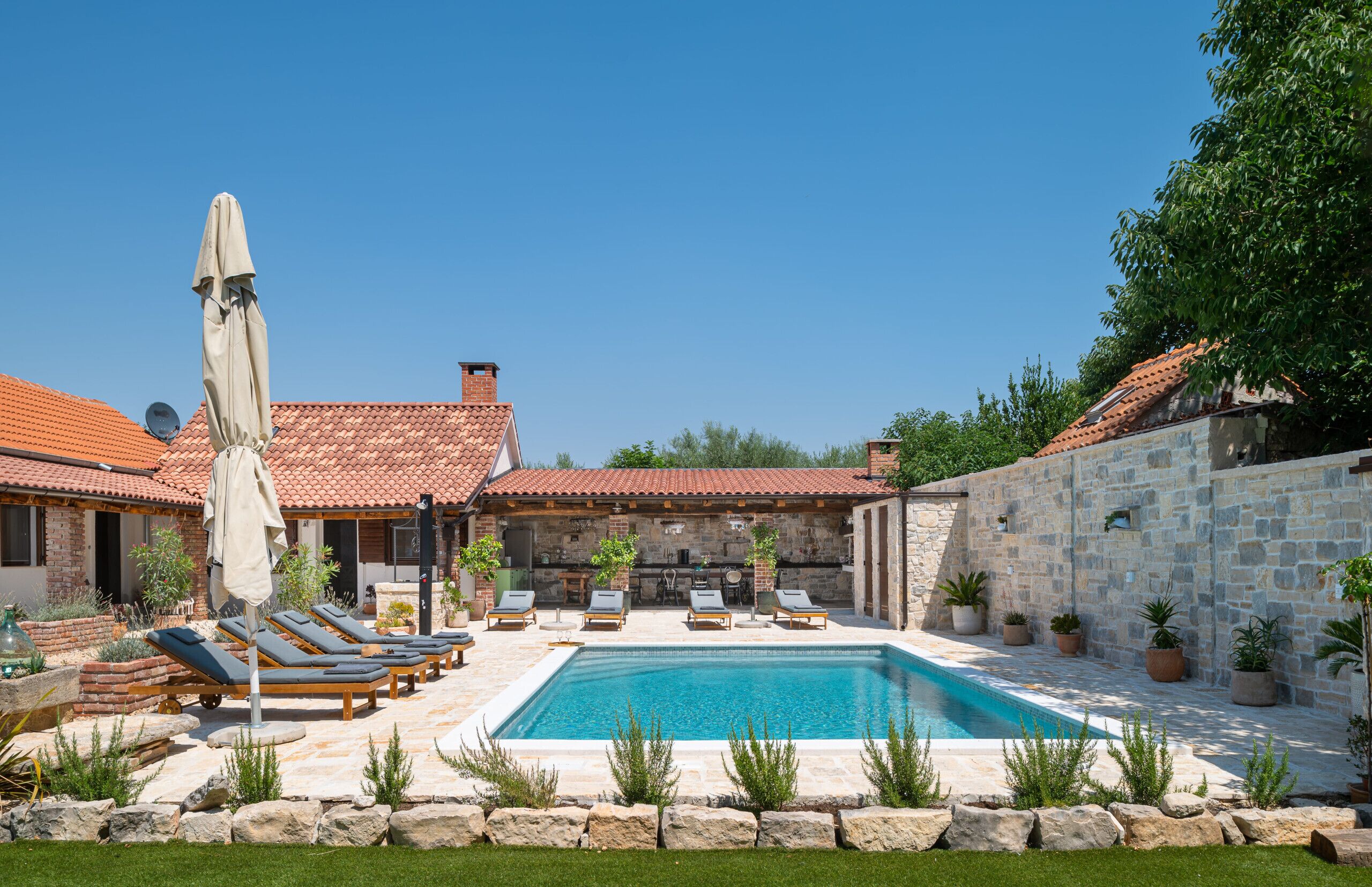 A poolside area with lounge chairs, a stone wall, and potted plants.