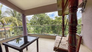 Un balcon avec une table et des chaises en verre, une balançoire et une vue sur la verdure et les bâtiments.
