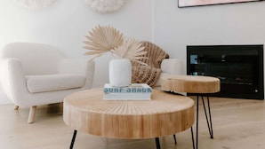 Un salon moderne avec un canapé blanc, une table basse ronde en bois sur laquelle sont posés des livres, et une cheminée.