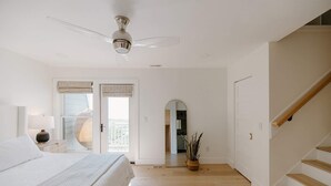 Une chambre à coucher avec un lit, un ventilateur de plafond, une fenêtre donnant sur un beau paysage, un miroir et un escalier.