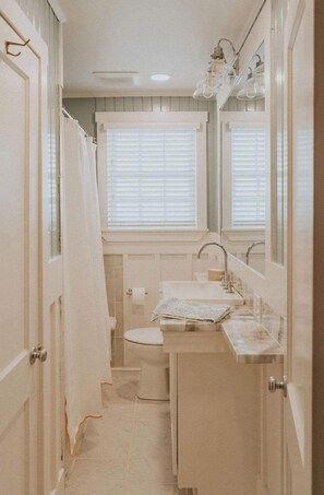 A compact bathroom with a toilet, sink, and mirror. - Palmetto Cottage (Wrightsville Beach)