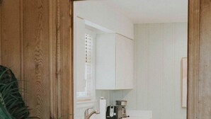 Cocina estrecha con armarios blancos, un lavabo y una cafetera.