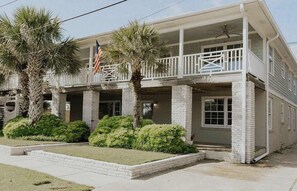 A two-story building with a balcony, stone pillars, and a flag. - Palmetto Cottage (Wrightsville Beach)