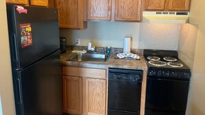 A compact kitchen with wooden cabinets, a black refrigerator, a dishwasher, a stove, and a microwave. - Free Ticket to Dollywood, Anakeesta, and Other Area Attractions! (Gatlinburg)
