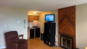 A living room with a brown armchair, a television on a stand, a fireplace, and a kitchen area with wooden cabinets and appliances. - Free Ticket to Dollywood, Anakeesta, and Other Area Attractions! (Gatlinburg)