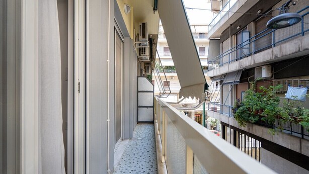 Varanda estreita com grades de metal, aparelhos de ar condicionado e vista para edifícios vizinhos.