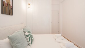 Quarto com cama, almofadas, luminária pendente e porta.