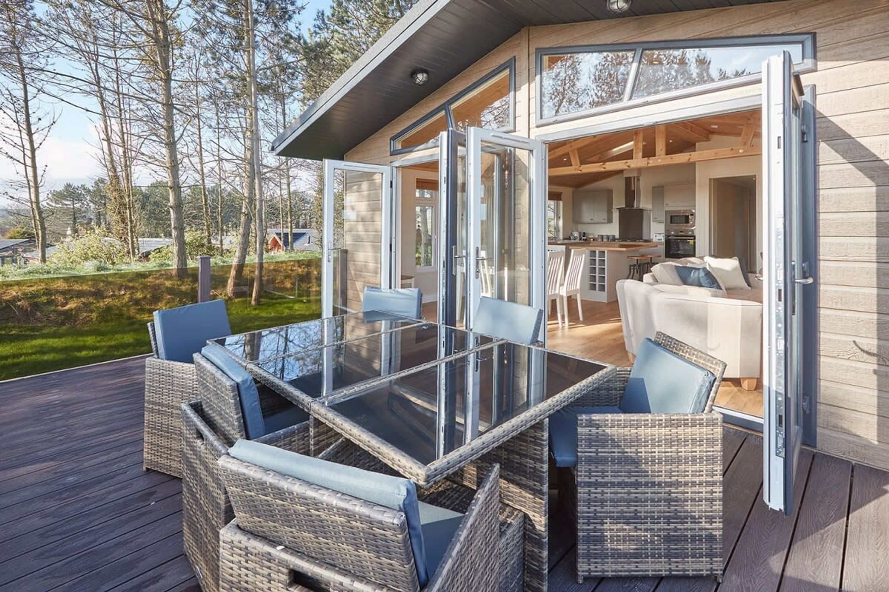 A modern outdoor dining area with wicker furniture and glass-top tables, connected to a cozy interior with a kitchen and seating area.