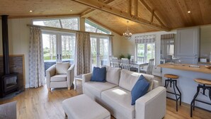 A cozy living room with a sofa, ottoman, and a fireplace. There is a dining area with a table and chairs, and a kitchen area with a bar counter and stools. - Host Stay Salt Seaweed (Saltburn-by-the-Sea)
