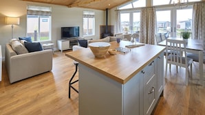 A spacious living area with a wooden ceiling, a central island with a bowl, a sofa, a TV, and a dining table with chairs. - Host Stay Salt Seaweed (Saltburn-by-the-Sea)