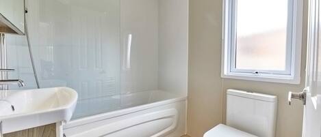 Un baño con ducha de vidrio, lavamanos blanco y retrete.