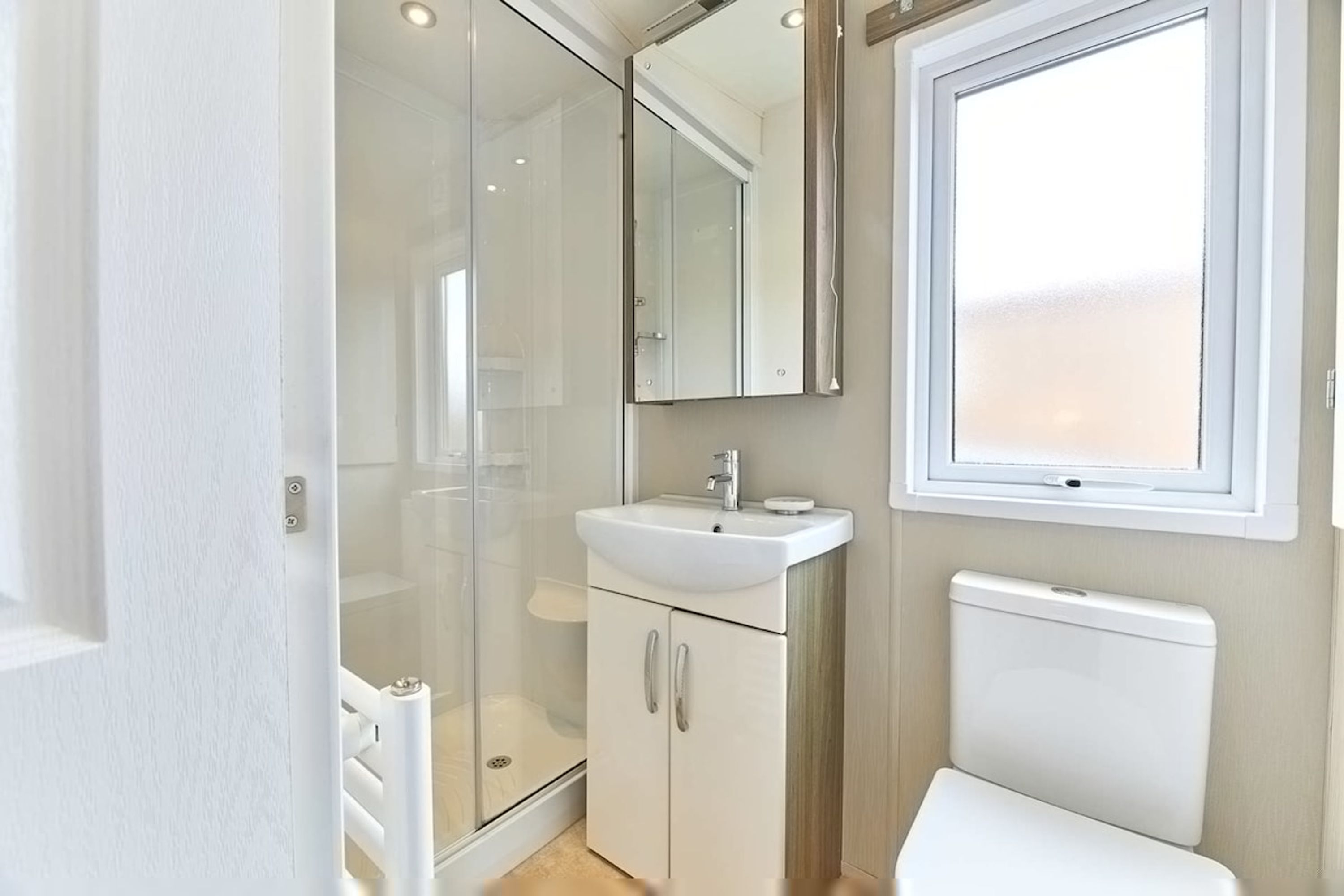 A modern bathroom with a glass shower enclosure, a white sink, a toilet, and a large mirror.