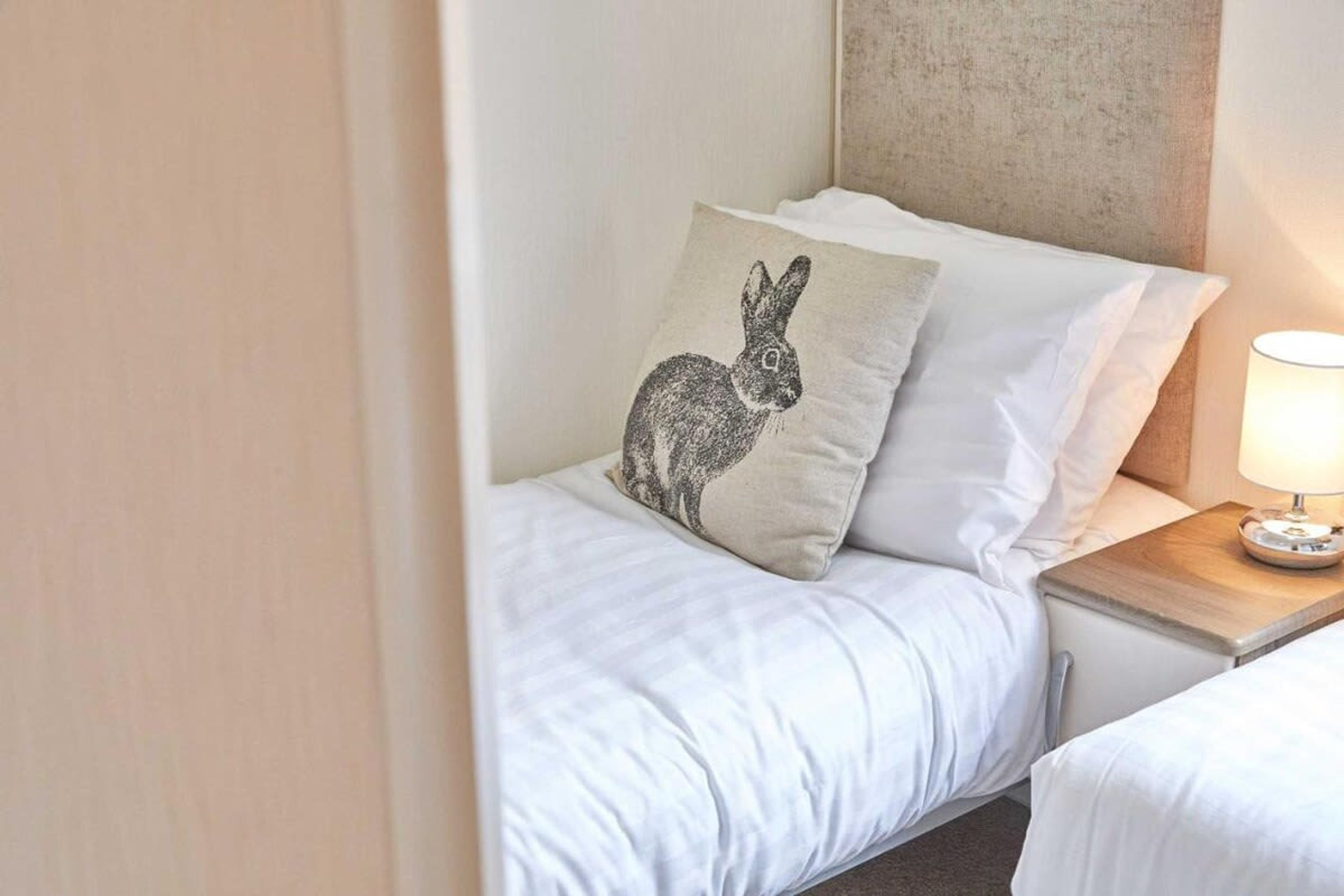 A neatly made bed with white bedding and a pillow featuring a rabbit design.