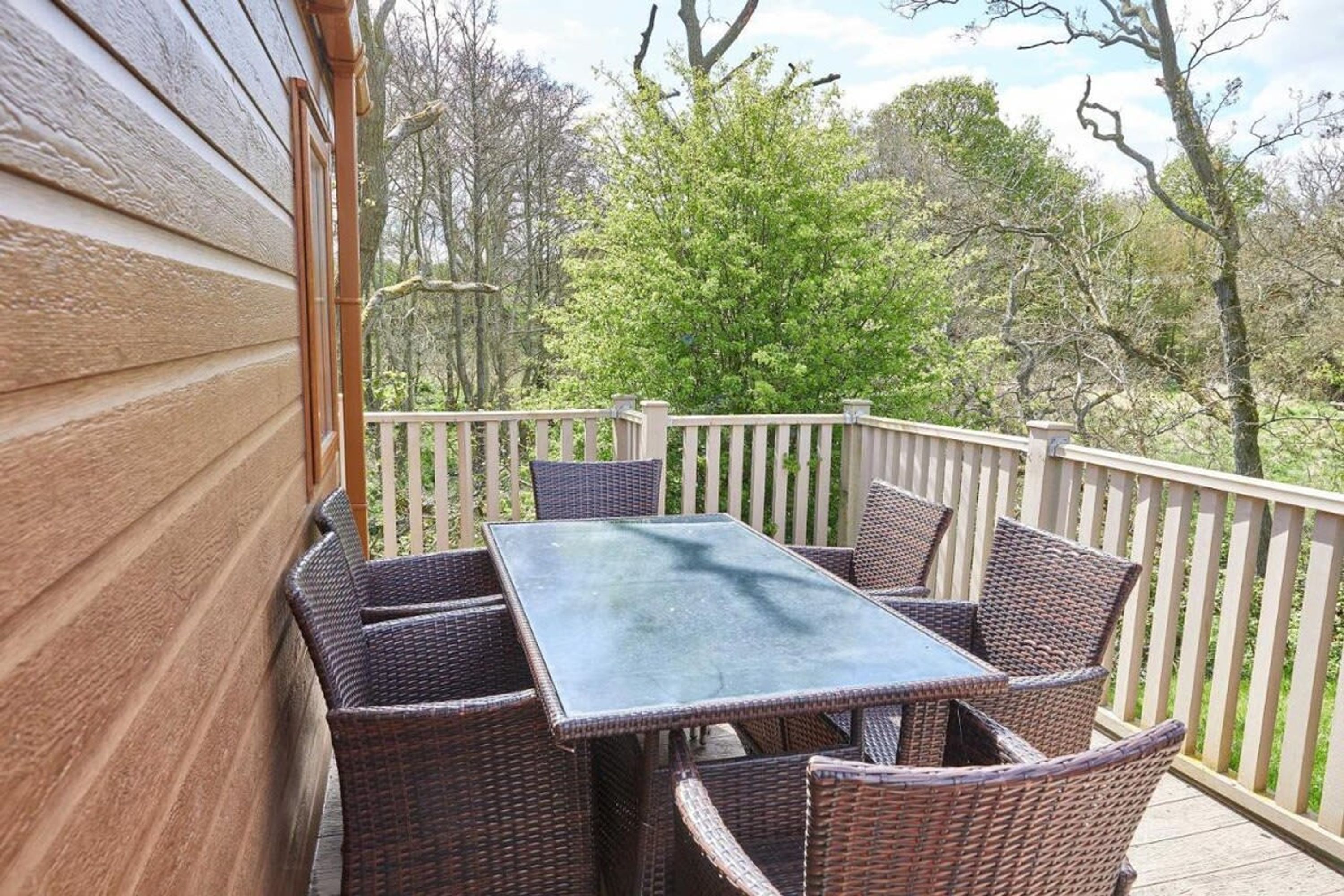 A covered patio with a table and chairs, surrounded by a wooden fence and trees.