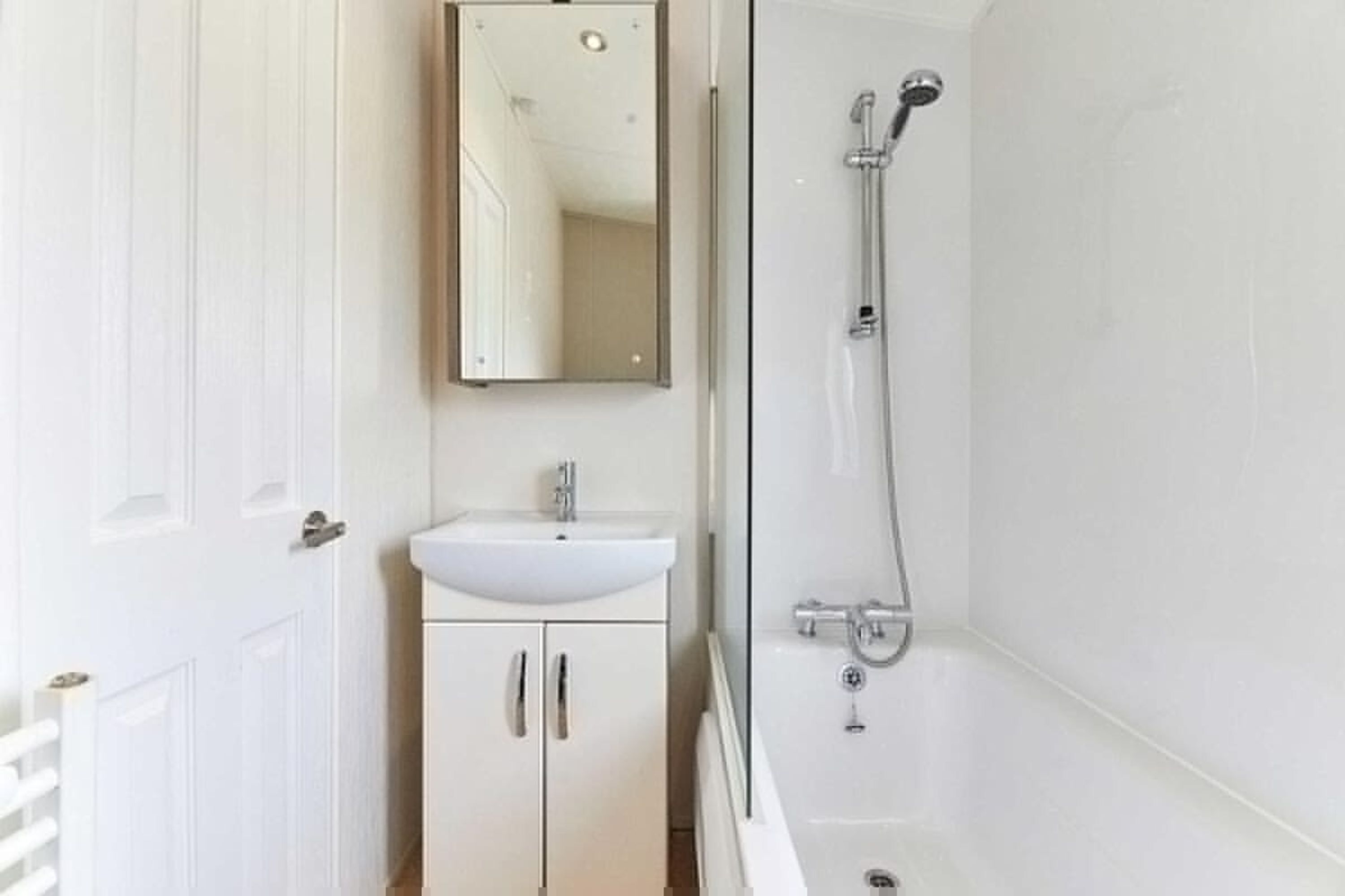 A bathroom with a white sink, mirror, and shower.