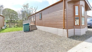A single-story wooden cabin with a gravel driveway, a green trash bin, and a clear sky. - Host Stay Yolo Lodge (Morpeth)