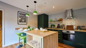 A modern kitchen with a wooden island, green bar stools, and a large window. - Host Stay Forest Green Lodge (Alnwick)
