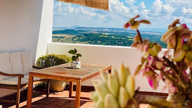 Une terrasse offrant une vue sur le paysage, une table agrémentée d’une plante en pot, une chaise et une lanterne.