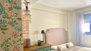 Une chambre avec une commode verte, une tête de lit rose et un papier peint à motifs floraux.