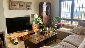 Un salon équipé d’un téléviseur, d’une table basse en bois, d’un canapé et d’une grande fenêtre donnant sur un beau paysage.