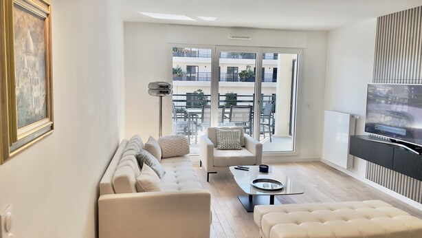 A modern living room with a sofa, ottoman, and a TV mounted on the wall.