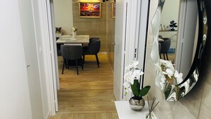 A hallway with a white console table, a mirror, and a dining area in the background.