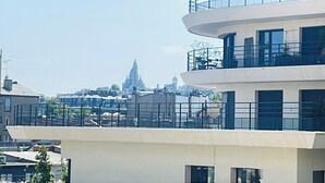 A multi-story building with balconies and a view of a distant church spire.