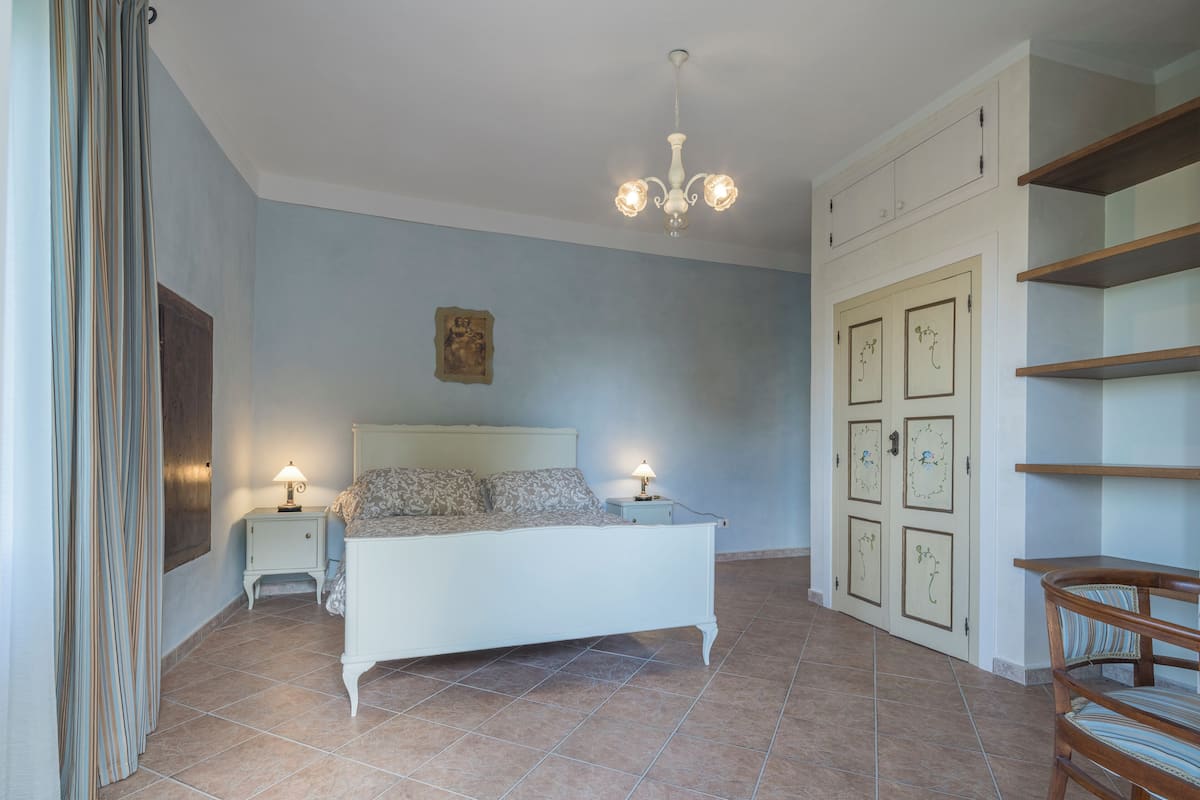 Une chambre à coucher comprenant un lit, des tables de chevet, un lustre, une chaise en bois et une armoire à portes.