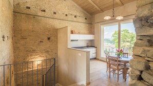 A rustic kitchen with stone walls, a wooden dining table with chairs, and a balcony with a view of the landscape. - Arpusè Relax nelle Langhe Barolo with Pool (Monforte d'Alba)