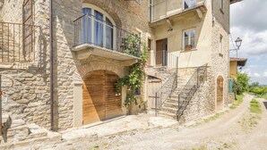 A stone building with a wooden door, a balcony with flowers, and a staircase leading to an upper floor. - Arpusè Relax nelle Langhe Barolo with Pool (Monforte d'Alba)