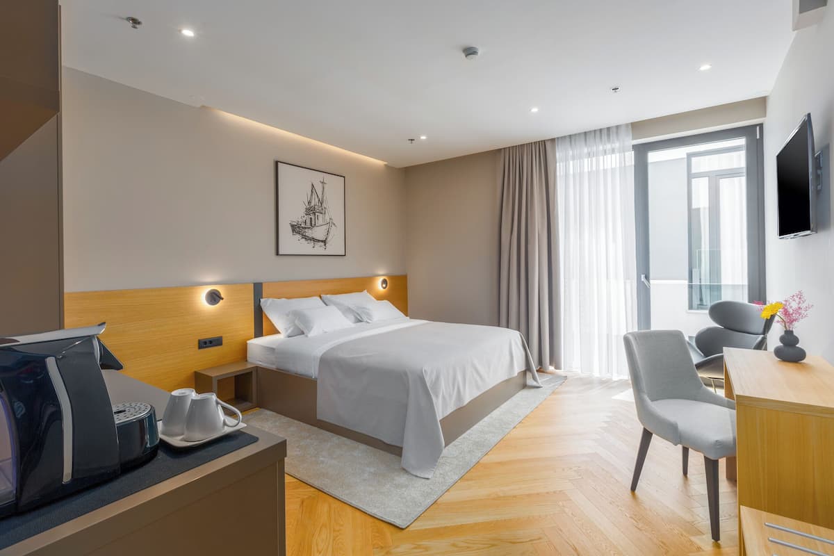 A modern hotel room with a neatly made bed, a desk with a chair, a coffee maker, and a flat-screen TV.