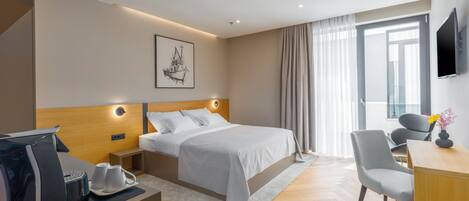 Una habitación de hotel moderna con una cama bien hecha, un escritorio con silla, cafetera y televisor de pantalla plana.