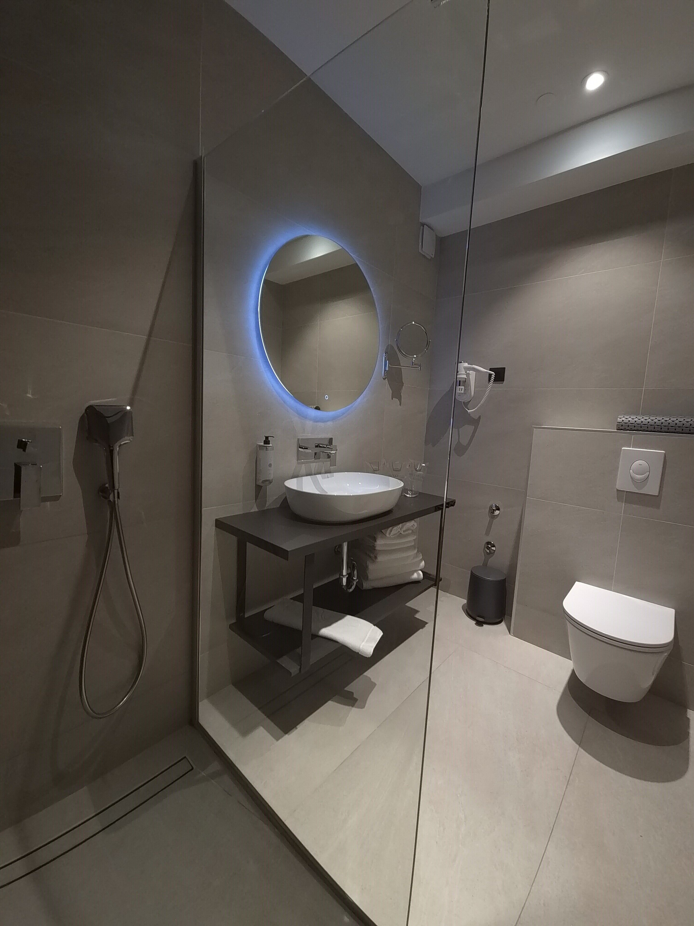 Une salle de bain moderne avec un miroir rond, un lavabo, des toilettes et une douche.