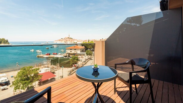 A balcony with a wooden floor, a round table with a potted plant, and two chairs. - Hotel Squero (Rovinj)