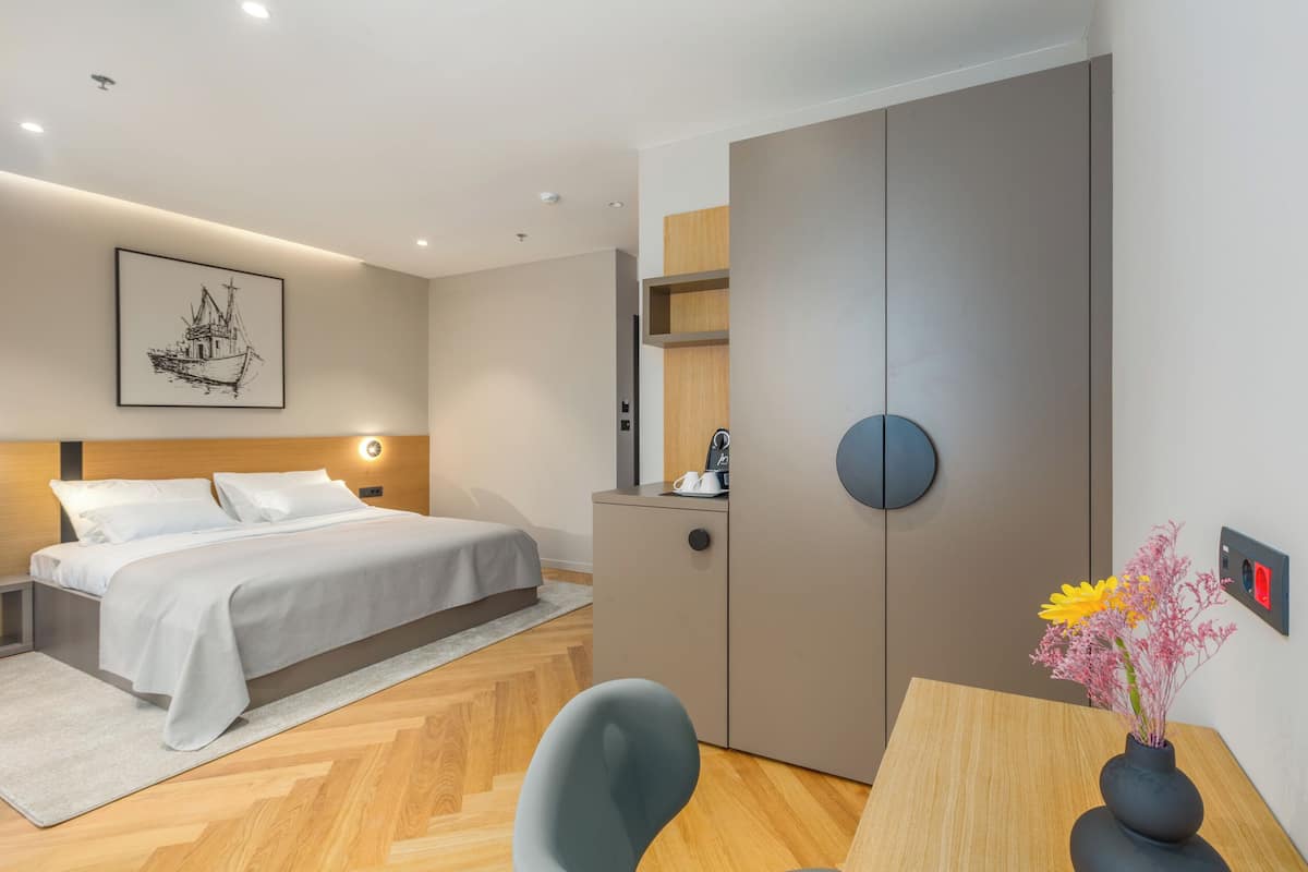 A modern hotel room with a bed, bedside table, desk, and a vase with flowers.