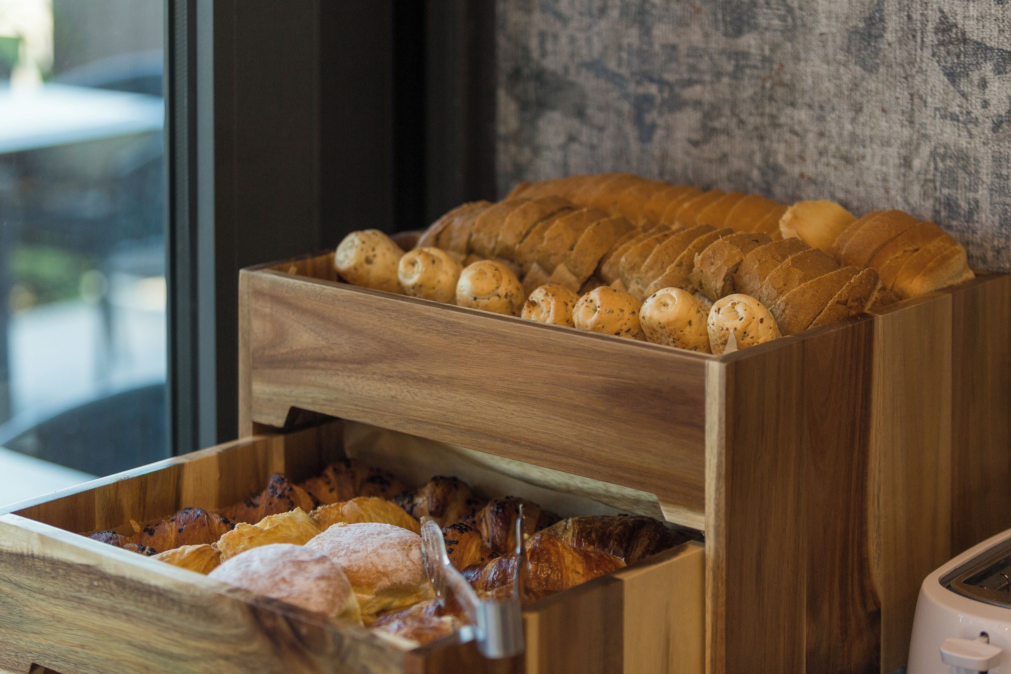A wooden bread display with various types of bread and pastries.