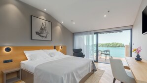 A modern bedroom with a large bed, a desk, and a view of the sea. - Hotel Squero (Rovinj)