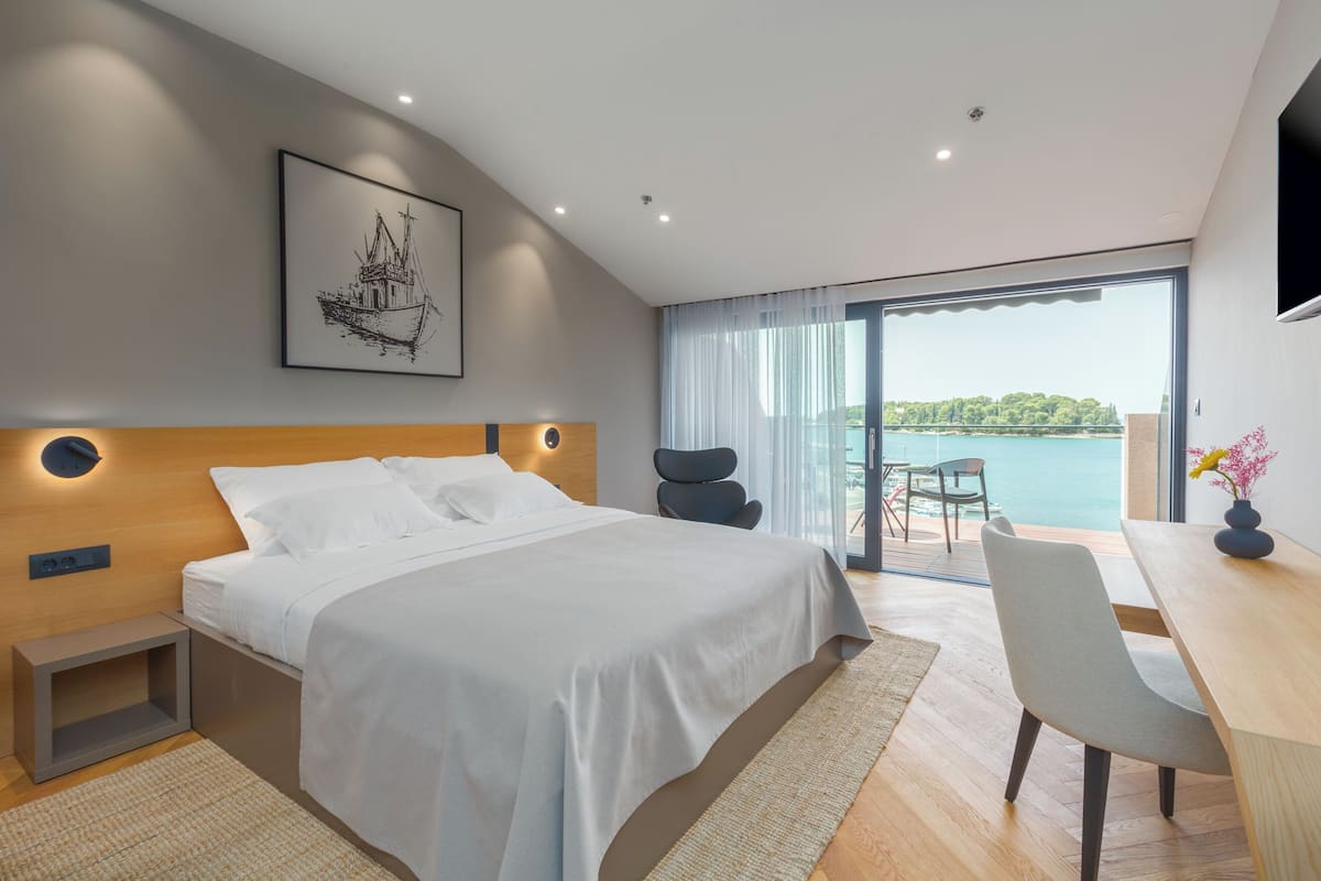 A modern bedroom with a large bed, a desk, and a view of the sea.
