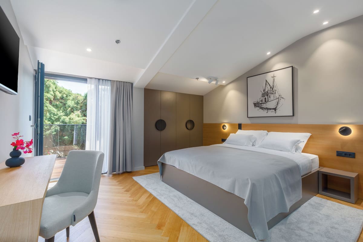A modern bedroom with a large bed, a desk with a chair, a TV, and a balcony with curtains.