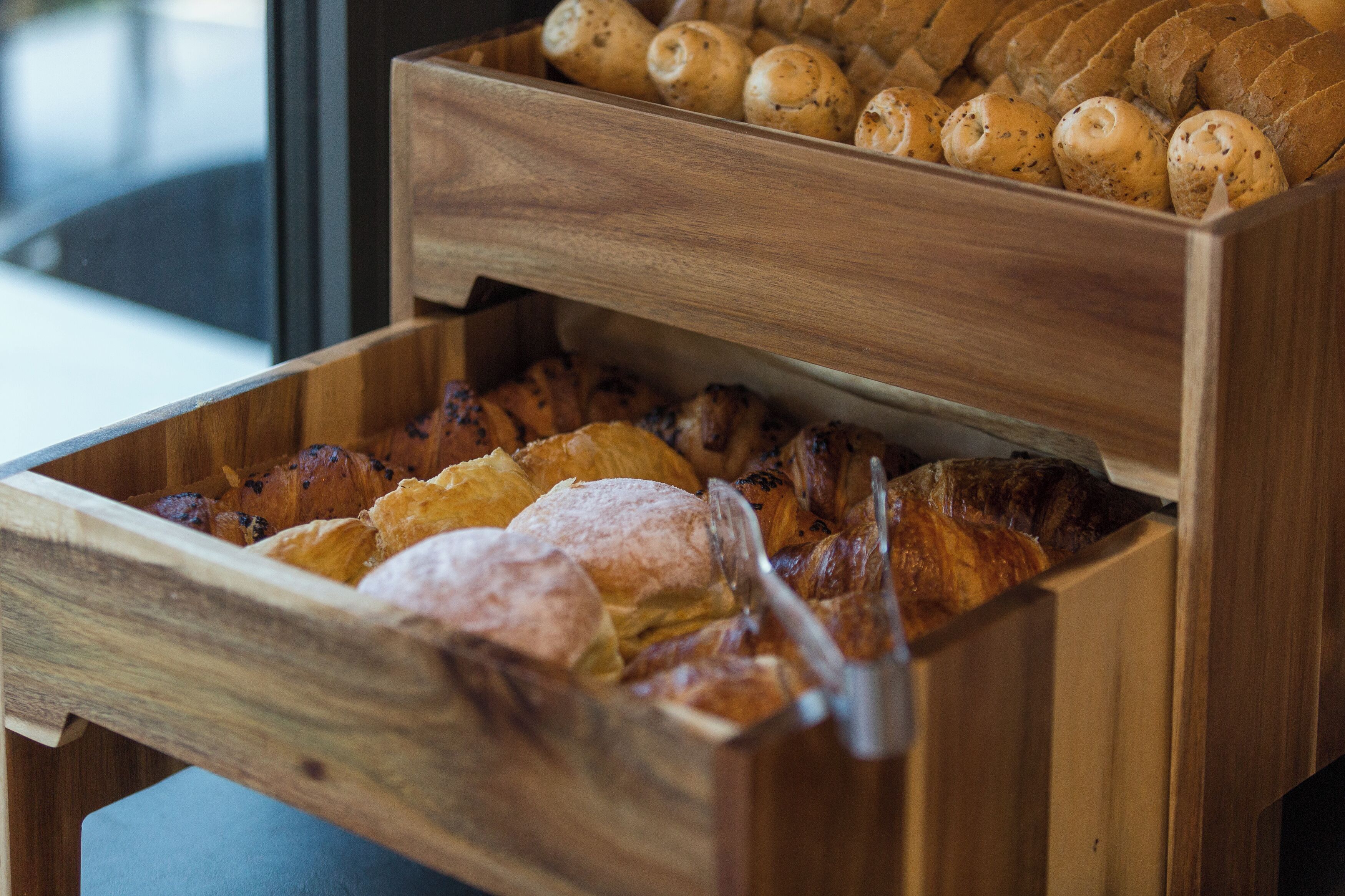 A wooden bread box with various types of bread inside.