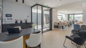A modern reception area with a glass door entrance, a reception desk with a laptop, and a seating area with tables and chairs. - Hotel Squero (Rovinj)