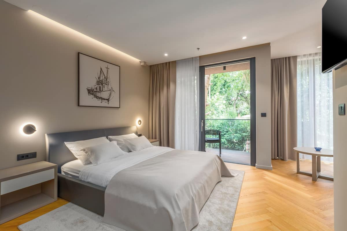 A modern bedroom with a large bed, bedside tables, a flat-screen TV, and a balcony with curtains.