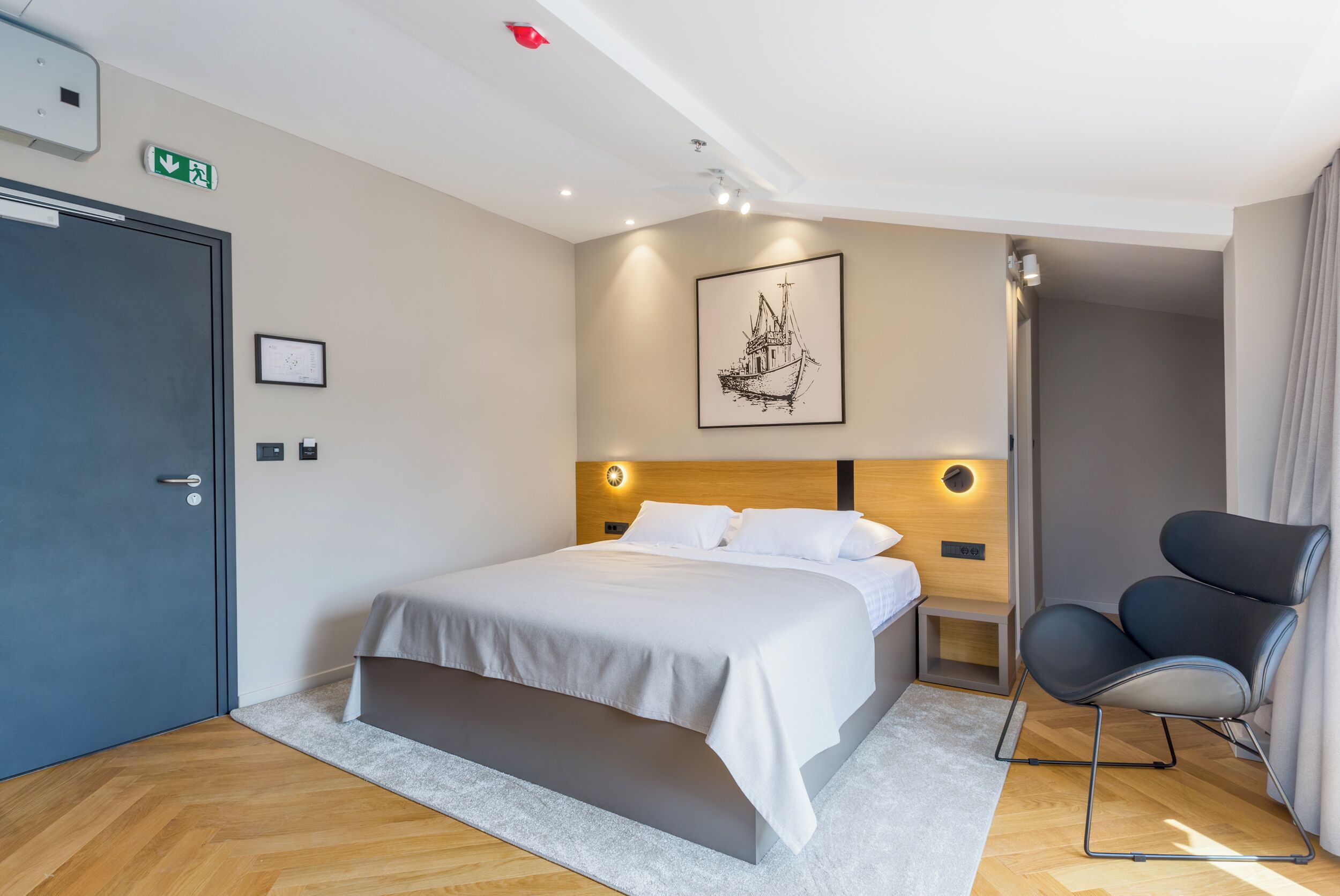 Ein Hotelzimmer mit Bett, Stuhl, gerahmtem Bild, Holz-Kopfteil und einer Tür.