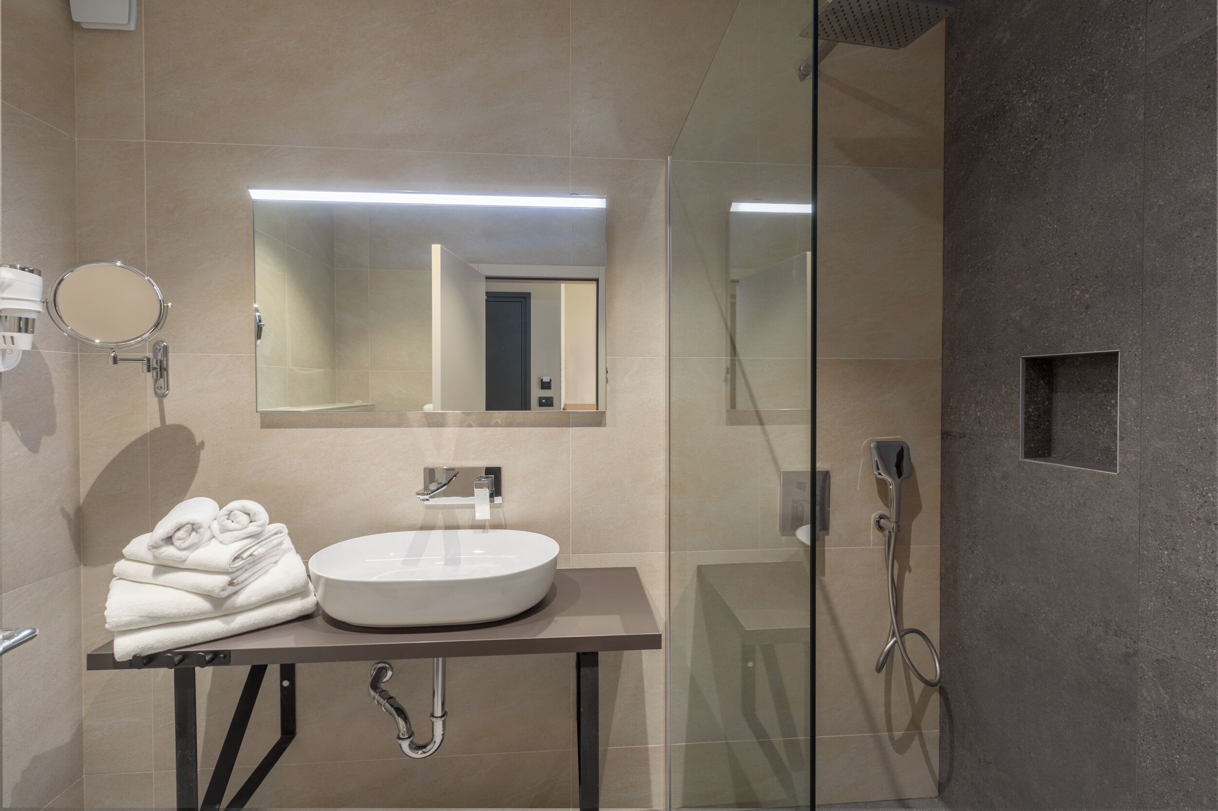 A modern bathroom with a round mirror, a white sink, and a glass shower enclosure.