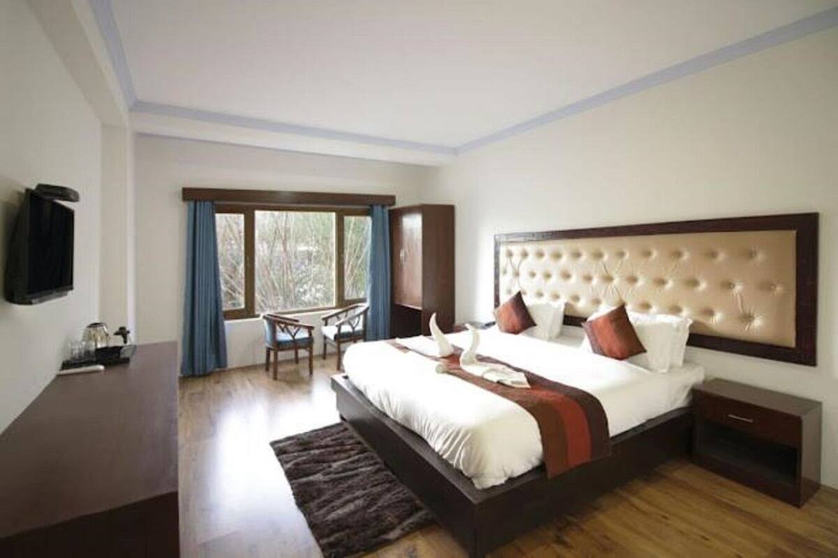 A bedroom with a large bed, a desk, and a television on the wall.