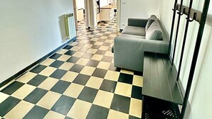 A hallway with a checkered floor, a sofa, a coat rack, and a door leading to another room. - ANCIENT GENOESE ATTIC (Genova)